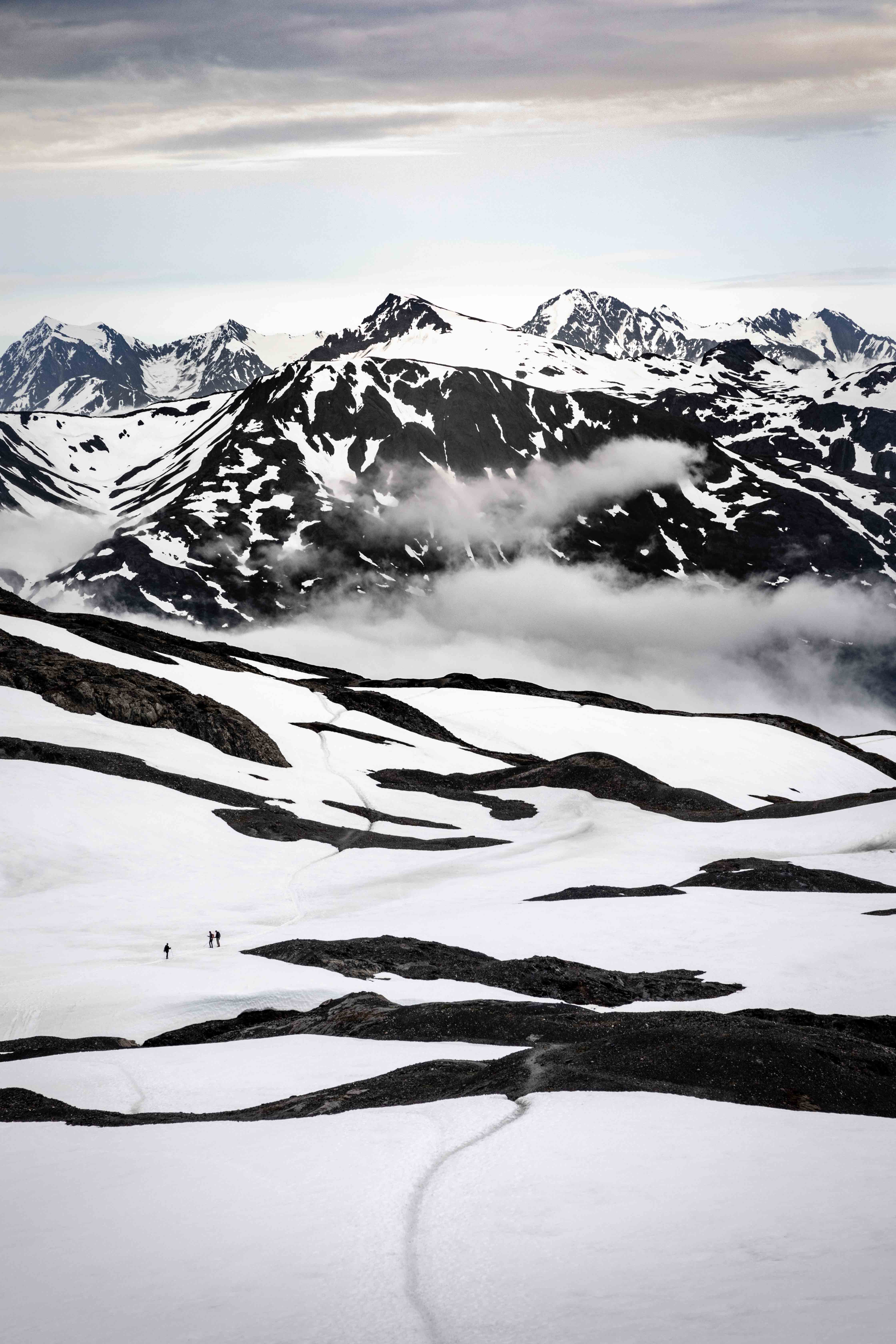 Hikers crossing a glacial snowfield with peaks behind
