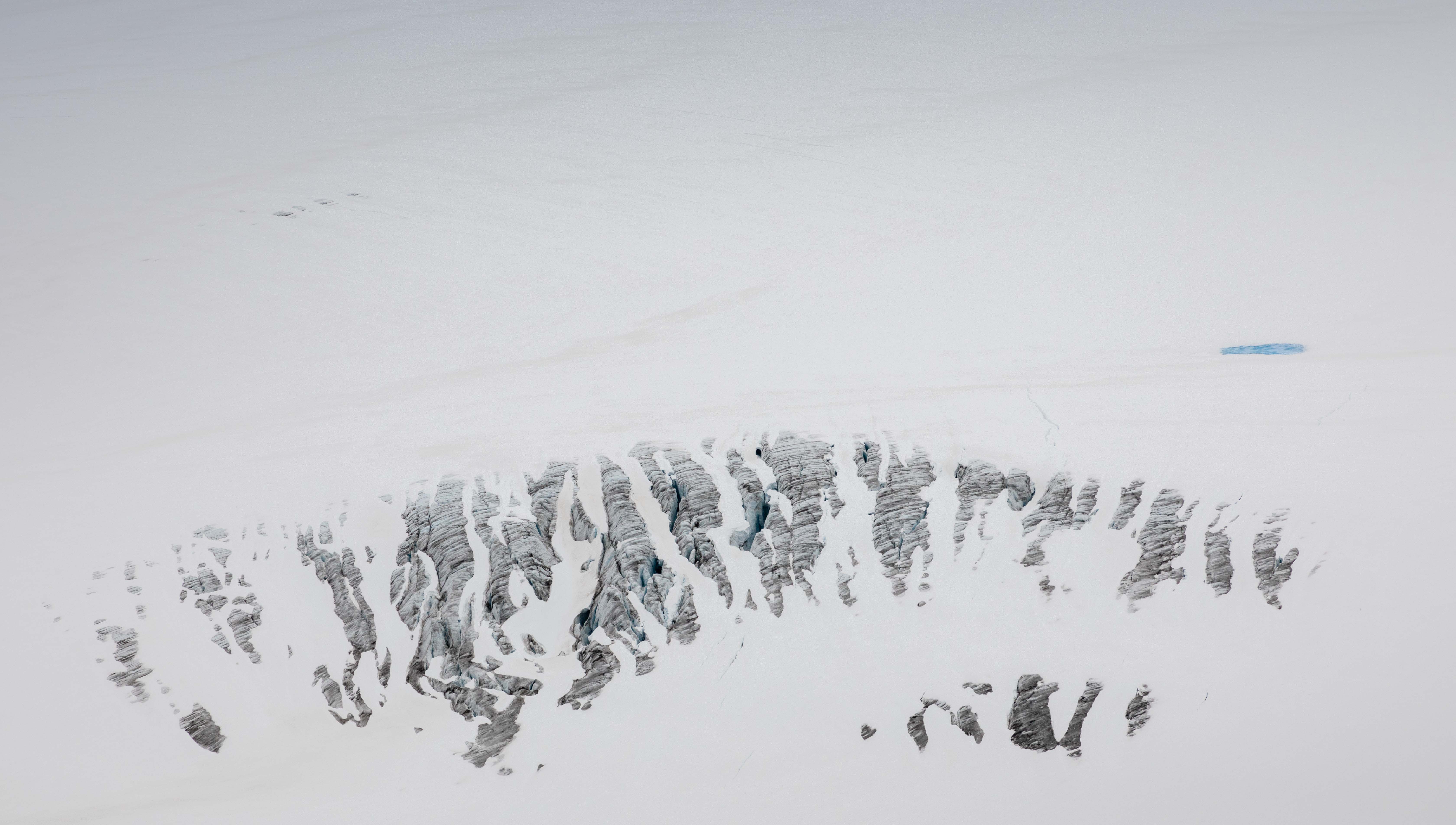 Glacier crevasses from above with a blue meltwater pool